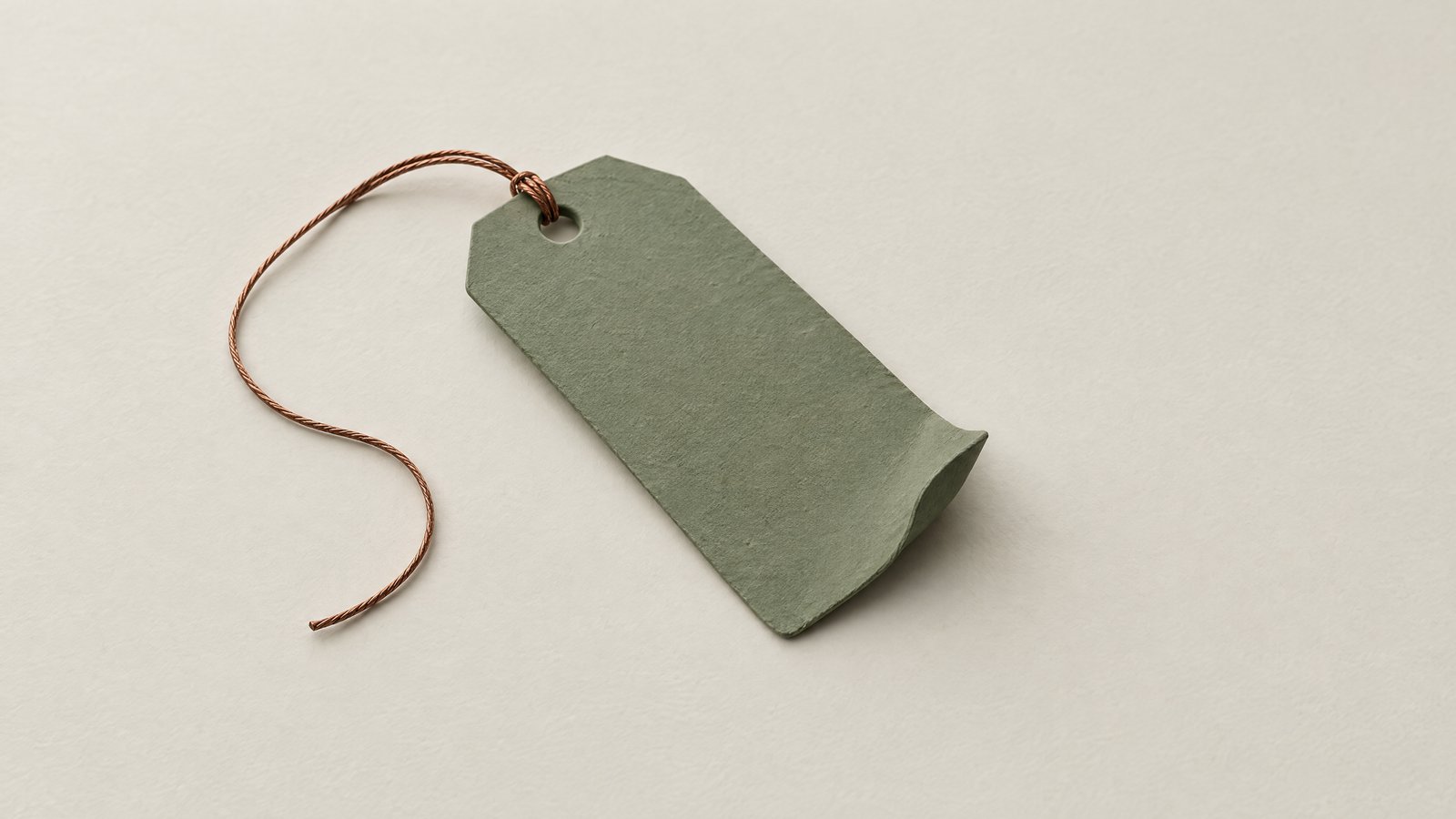 A blank sage green price tag with a curled corner and a slack copper string